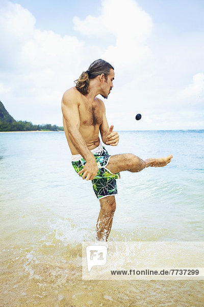 A man kicks a hackey sack while standing in the shallow water of the ocean Hawaii united states of america