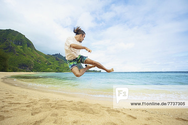 A man takes a leap into the air while playing with a hackey sack on the beach Hawaii united states of america