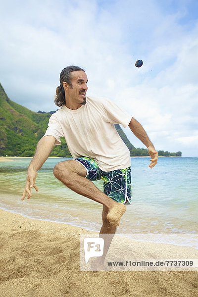 A man plays with his hackey sack in the sand at the water's edge Hawaii united states of america