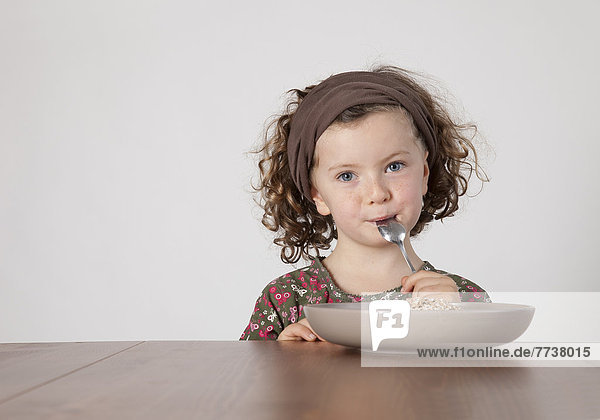 Mädchen sitzt am Tisch mit Löffel im Mund