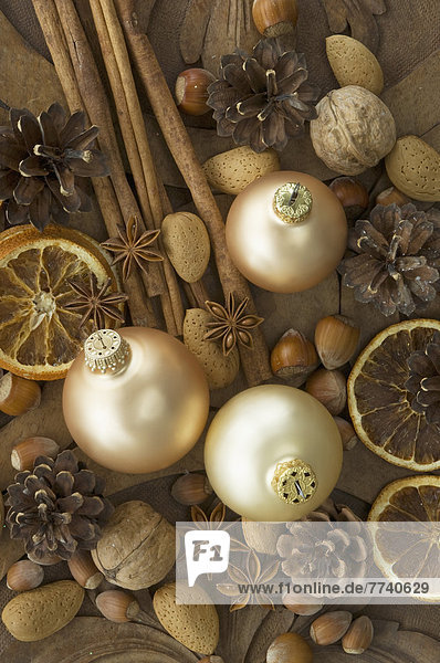 Weihnachtskugeln mit getrockneten Orangenscheiben  Zimtstangen  Walnüssen  Haselnüssen  Mandeln und Tannenzapfen auf Tisch