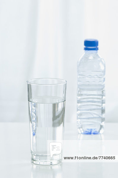 Mineralwasserglas mit Flasche im Hintergrund  Nahaufnahme