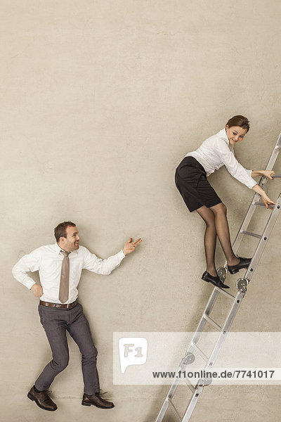 Businessman teasing while businesswoman climbing ladder in office