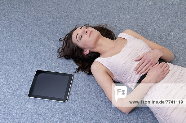 Erschöpfte Geschäftsfrau auf dem Boden neben dem digitalen Tablett liegend