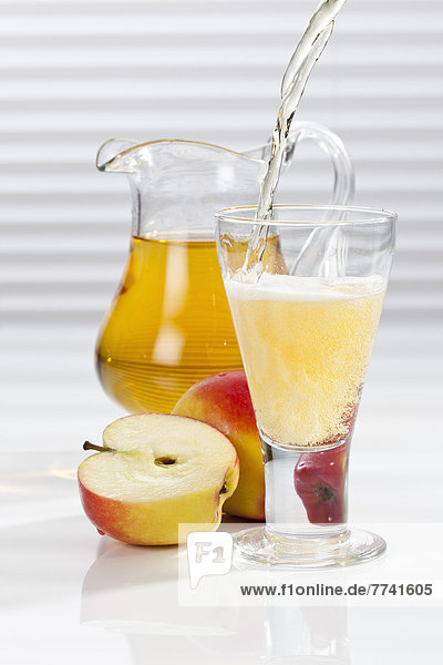 Apfelsaft wird neben Äpfeln und Krug ins Glas gegossen.