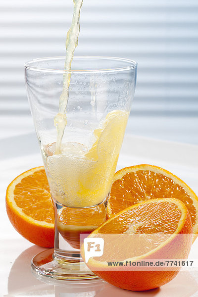 Orangenlimonade wird neben Orangen in Glas gegossen.