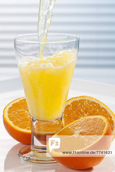 Orangenlimonade wird neben Orangen in Glas gegossen.