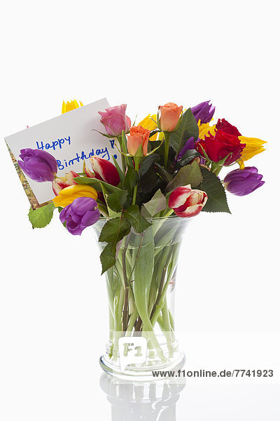 Variety of flowers in vase with birthday card on white background  close up