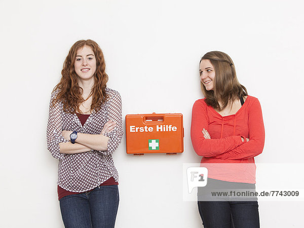 Portrait of young women leaning against wall with first aid kit  smiling