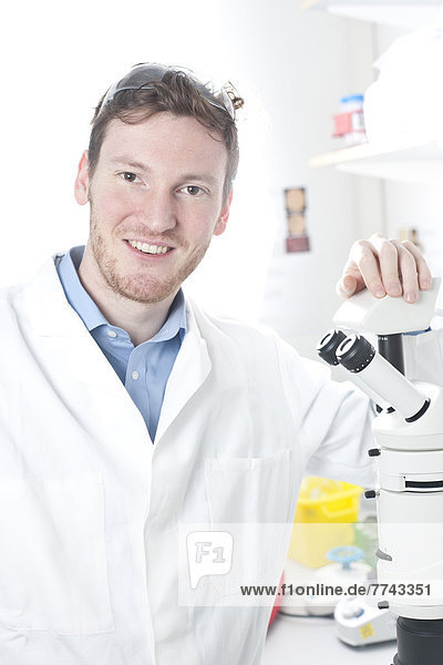 Deutschland  Porträt eines jungen Wissenschaftlers mit Mikroskop im Labor  lächelnd