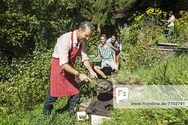 Österreich  Salzburger Land  Mann kocht für seine Familie im Garten