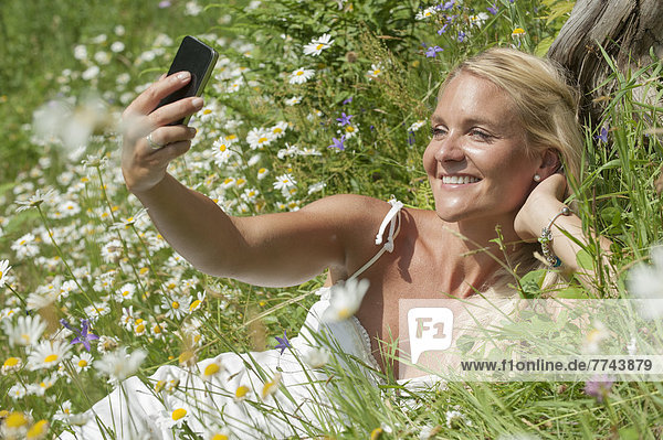 Österreich  Salzburg  Mittlere erwachsene Frau mit Handy auf der Wiese  lächelnd