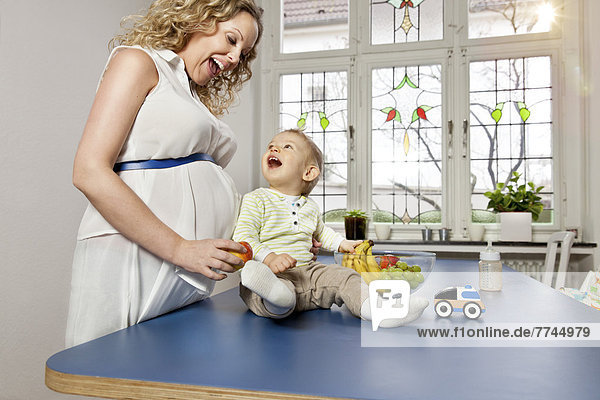 Deutschland  Bonn  Schwangere Mutter zeigt dem Sohn im Wohnzimmer Früchte  lächelnd