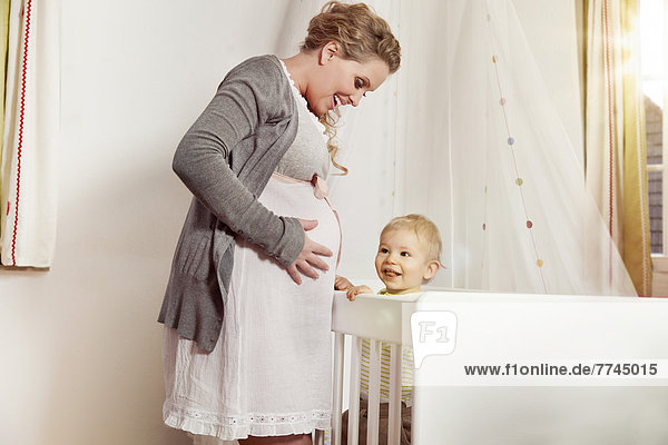 Germany  Bonn  Pregnant mother with son standing near his bed