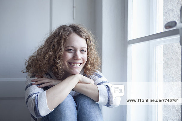 Junge Frau am Fenster sitzend  lächelnd  Porträt