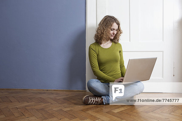 Junge Frau auf dem Boden sitzend und mit Laptop