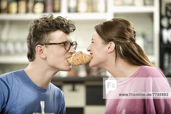 Junger Mann und Frau teilen sich Croissant im Cafe