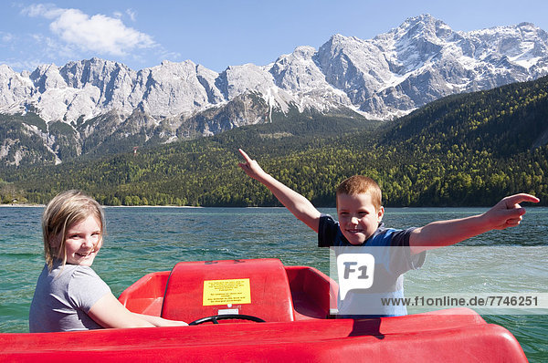 Boy and girl in paddleboat on Lake Eibsee with Zugspitze and Wetterstein mountains in background