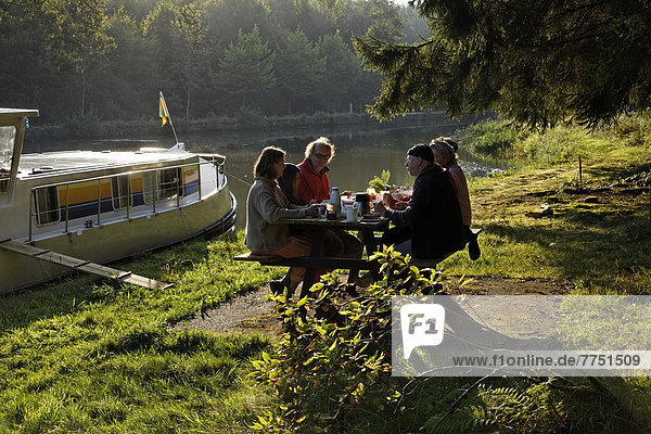 Holidaymakers having breakfast on a picnic table  morning mood  houseboat on the Canal des Vosges  formerly Canal de l'Est  landing in the forest at PK 115