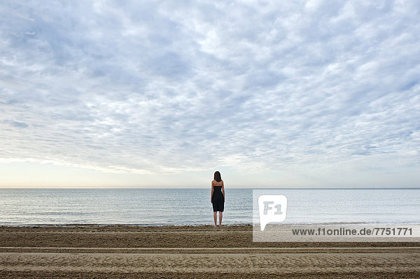 Woman wearing a black dress standing by the sea  moody clouds