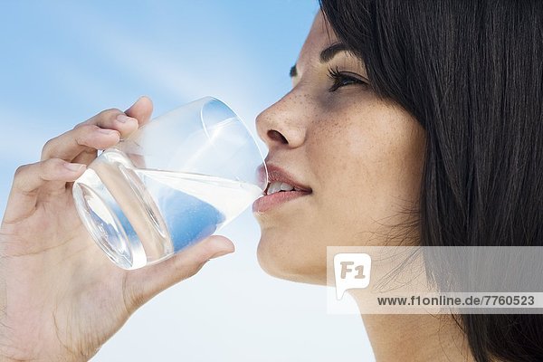 Braunhaarige junge Frau  die ein Glas Wasser trinkt.