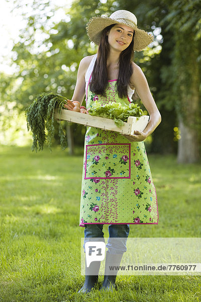 Junge Frau hält eine Kiste mit Gemüse.