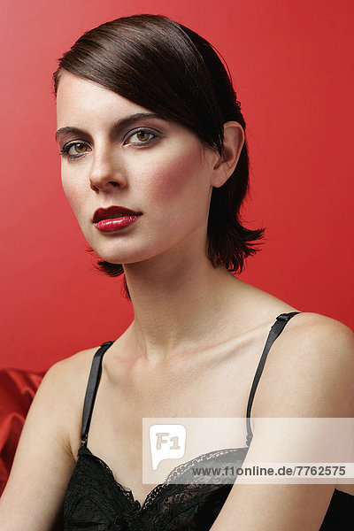 Porträt einer geschminkten Frau in schwarzem Spitzenoberteil für die Kamera  roter Hintergrund