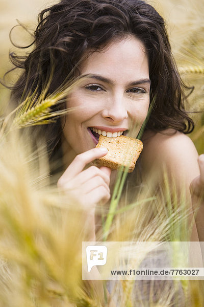 Junge Frau im Weizenfeld  die einen Zwieback isst.