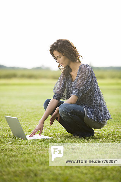 Young woman crouching in grass  using laptop computer