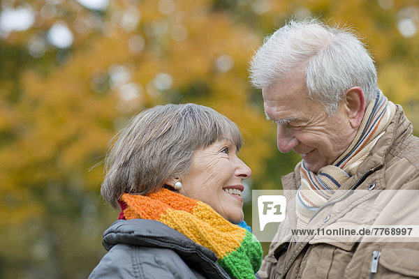 Seniorenpaar lächelt sich an  vor herbstlicher Laubbaumkulisse