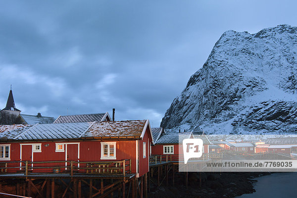 Fischerort mit roten Hütten am Fjord  bei Dämmerung  im Winter
