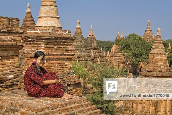 Young Burmese woman in a red dress sitting on the roof of a temple  Bagan (Pagan)  Myanmar (Burma)  Asia
