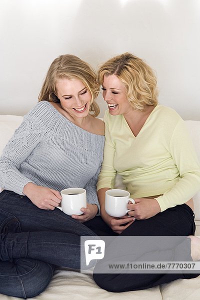 Two young women smiling  on sofa  holding cup of tea