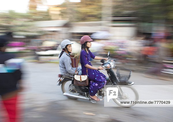 Panned and blurred shot  creating a sense of movement  of two women riding moped through a market  Mandalay  Myanmar (Burma)  Asia