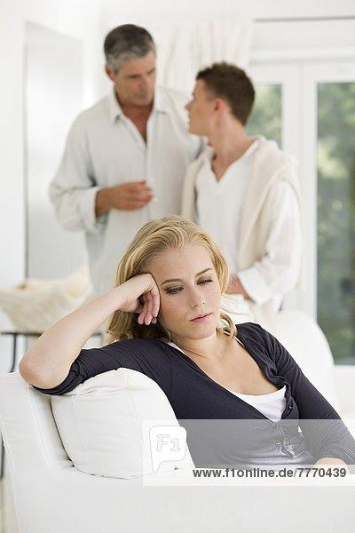 Junge Frau auf der Couch  Vater und Sohn diskutieren im Hintergrund