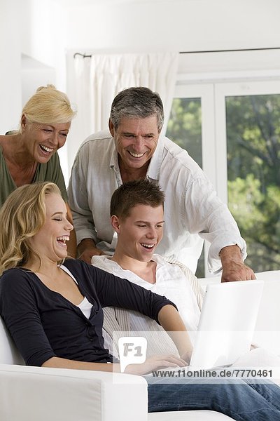Mature couple and young couple at home  looking at laptop
