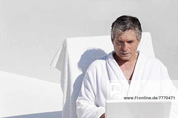 Senior man using a laptop  naer a pool