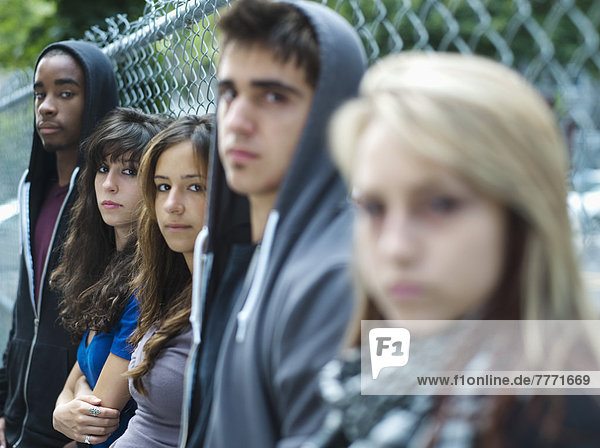 5 Teenager  die sich gegen den Kettengliederzaun lehnen