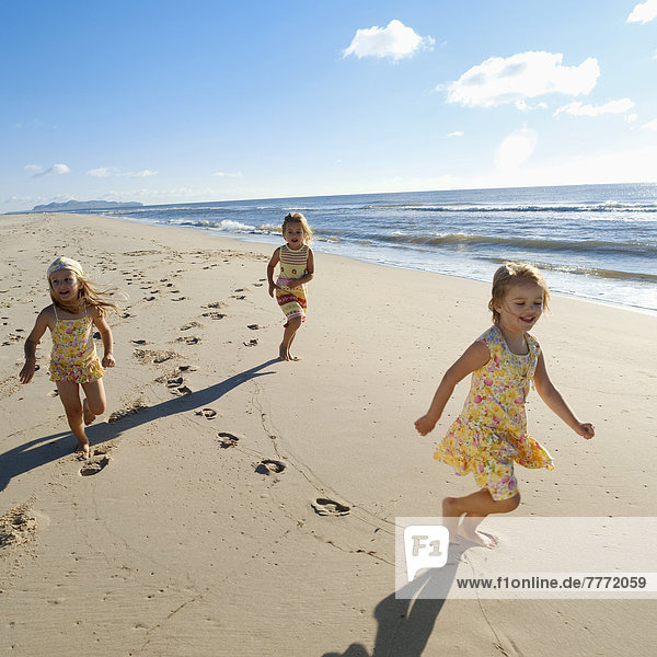Drei kleine Mädchen  die am Strand rennen.