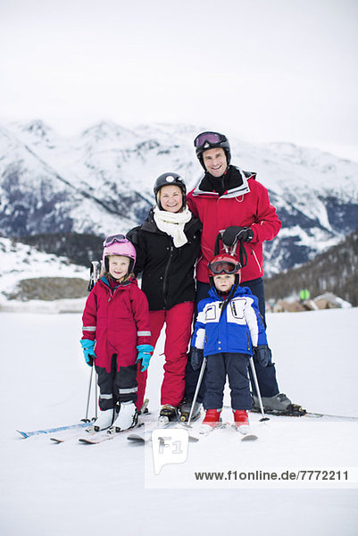 Porträt einer Familie in Skibekleidung,  die zusammen gegen die Bergkette steht.