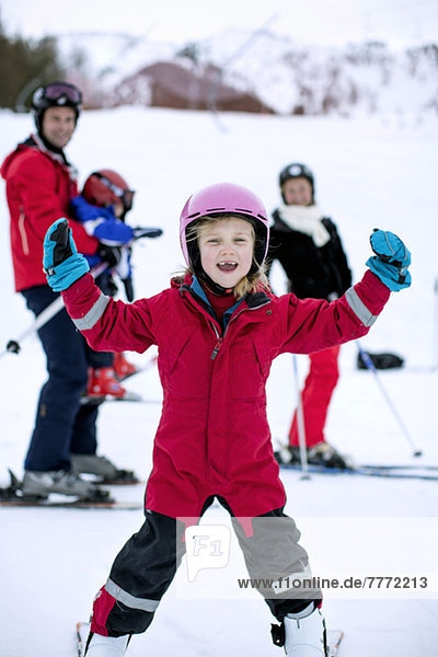 Portrait of happy girl enjoying skiing with family in background