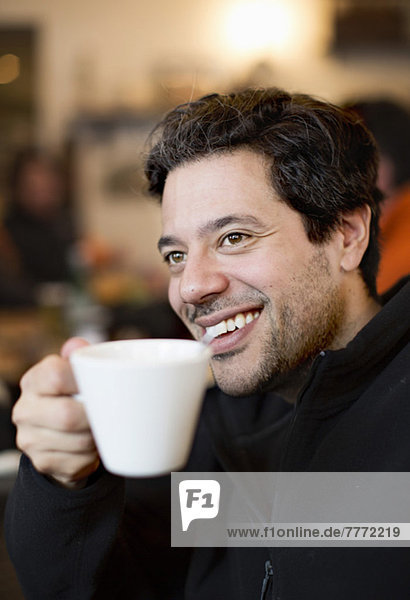 Fröhlicher erwachsener Mann schaut weg  während er eine Kaffeetasse hält.