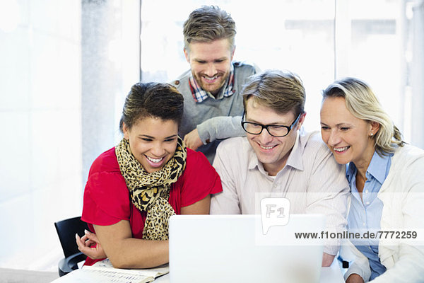 Happy business people using laptop together at desk