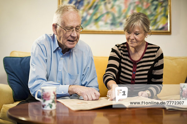 Senior couple reading newspaper together at coffee table
