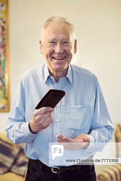 Porträt eines glücklichen älteren Mannes mit Brieftasche  der zu Hause steht.