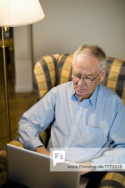 Senior Mann mit Laptop auf Sessel