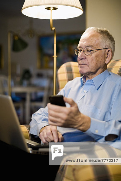 Senior-Mann mit Laptop  Handy und digitalem Tablett im Sessel