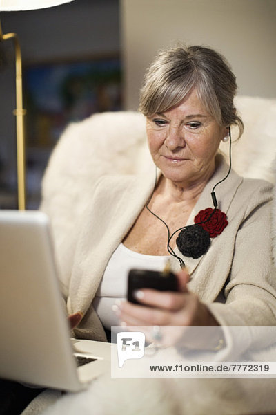 Seniorenfrau mit Laptop  die auf der Couch sitzt und Musik hört.