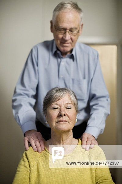 Entspannte Seniorin bei einer Schultermassage vom Mann zu Hause