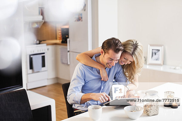 Glückliches Paar mit digitalem Tablett am Frühstückstisch